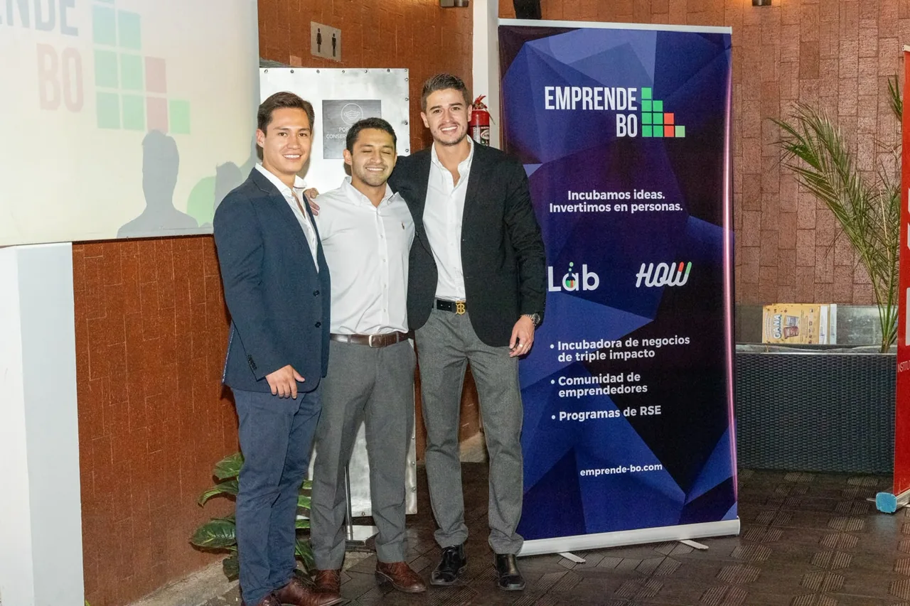Fotografía grupal de tres personas frente al banner de EmprendeBO.